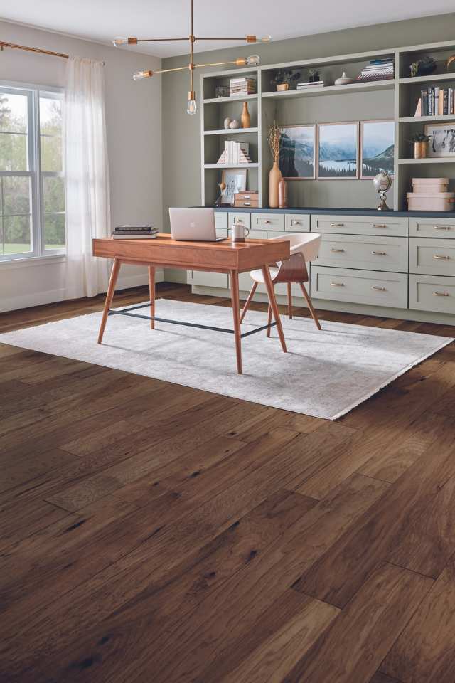 modern home office with area rug on hardwood flooring and sage green accent wall with custom built shelving